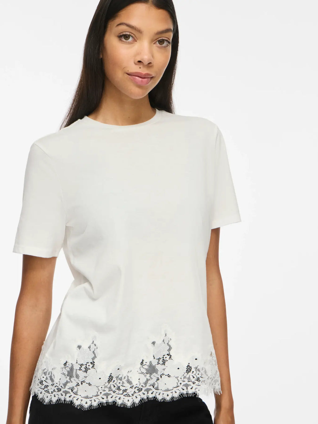 Modelo con camiseta blanca de manga corta y cuello redondo con encaje floral blanco semitransparente y borde de pestañas en el bajo