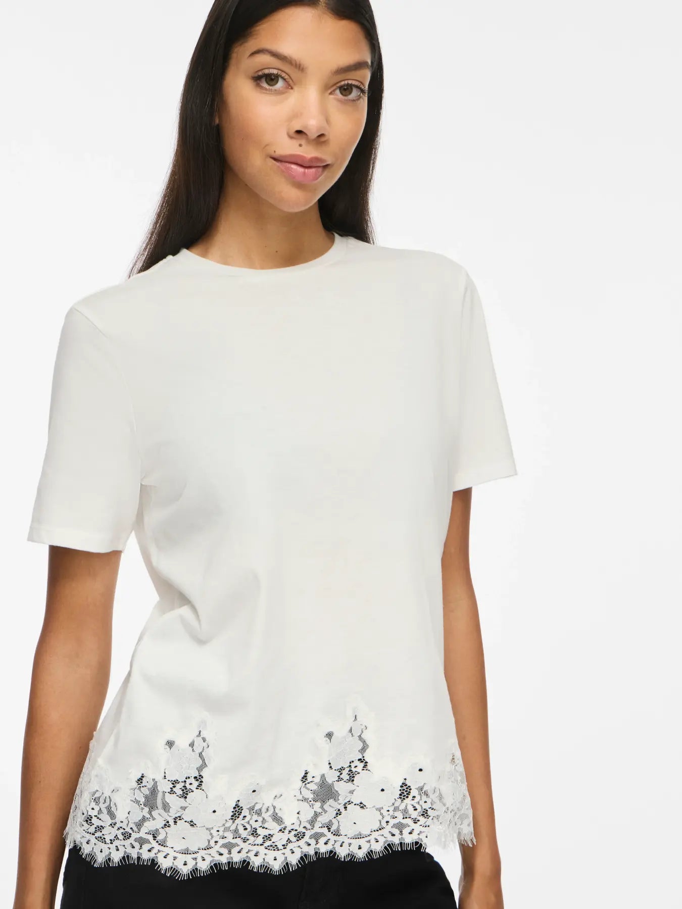 Modelo con camiseta blanca de manga corta y cuello redondo con encaje floral blanco semitransparente y borde de pestañas en el bajo