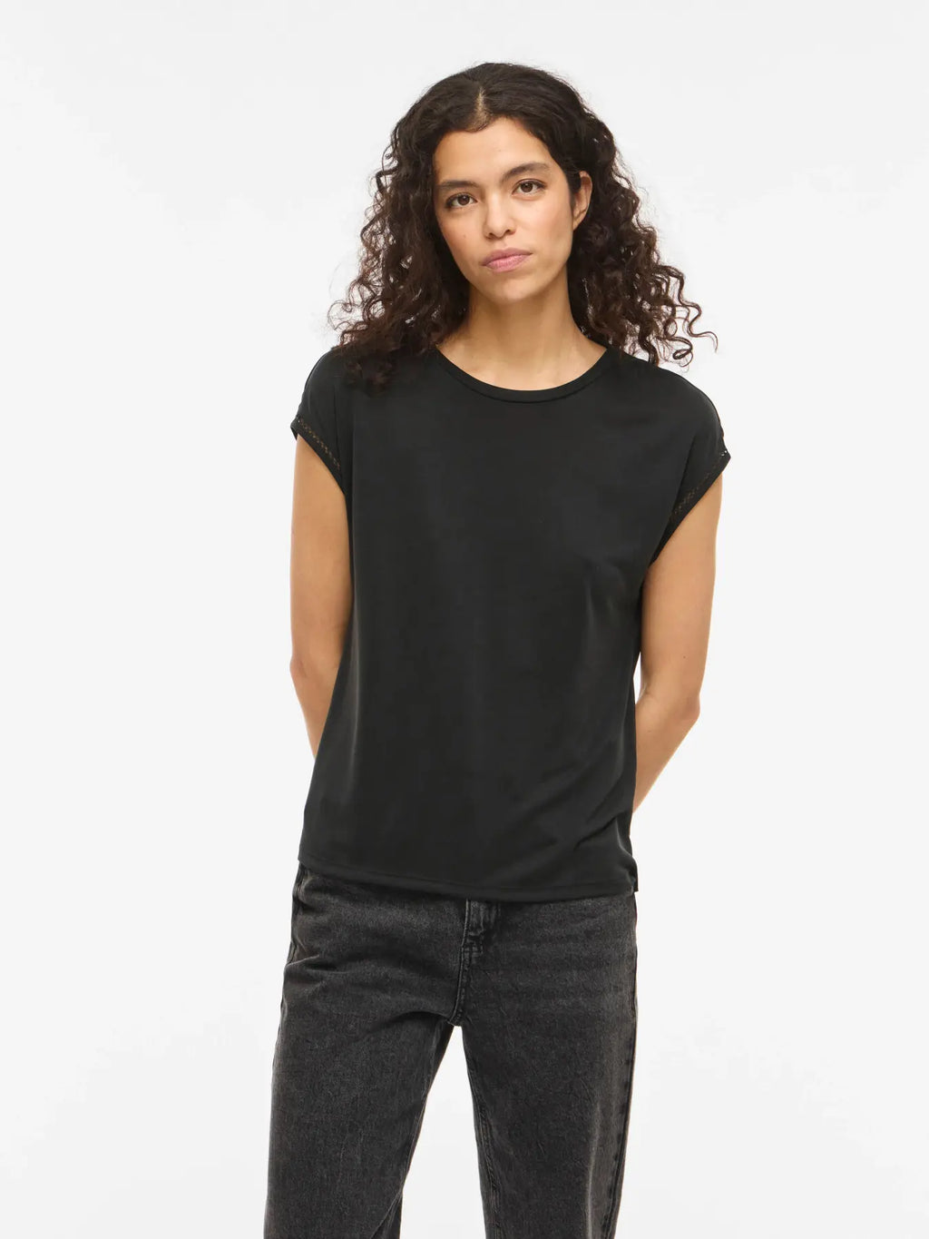 Camiseta Vila negra de manga caída y cuello redondo en tejido fluido, con detalle calado en el borde de la manga que aporta un acabado delicado y femenino. Ajuste recto y caída ligera.