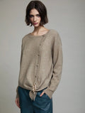 Cardigan Sienna de SKATIE en punto beige mélange con manga larga, botonadura lateral en diagonal, bajo asimétrico efecto pañuelo y broche metálico dorado