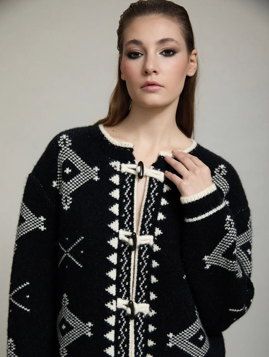 Detalle de la chaqueta de punto Zenda de SKATIE con estampado jacquard geométrico negro y crudo, ribete en contraste y cierres tipo alamar.