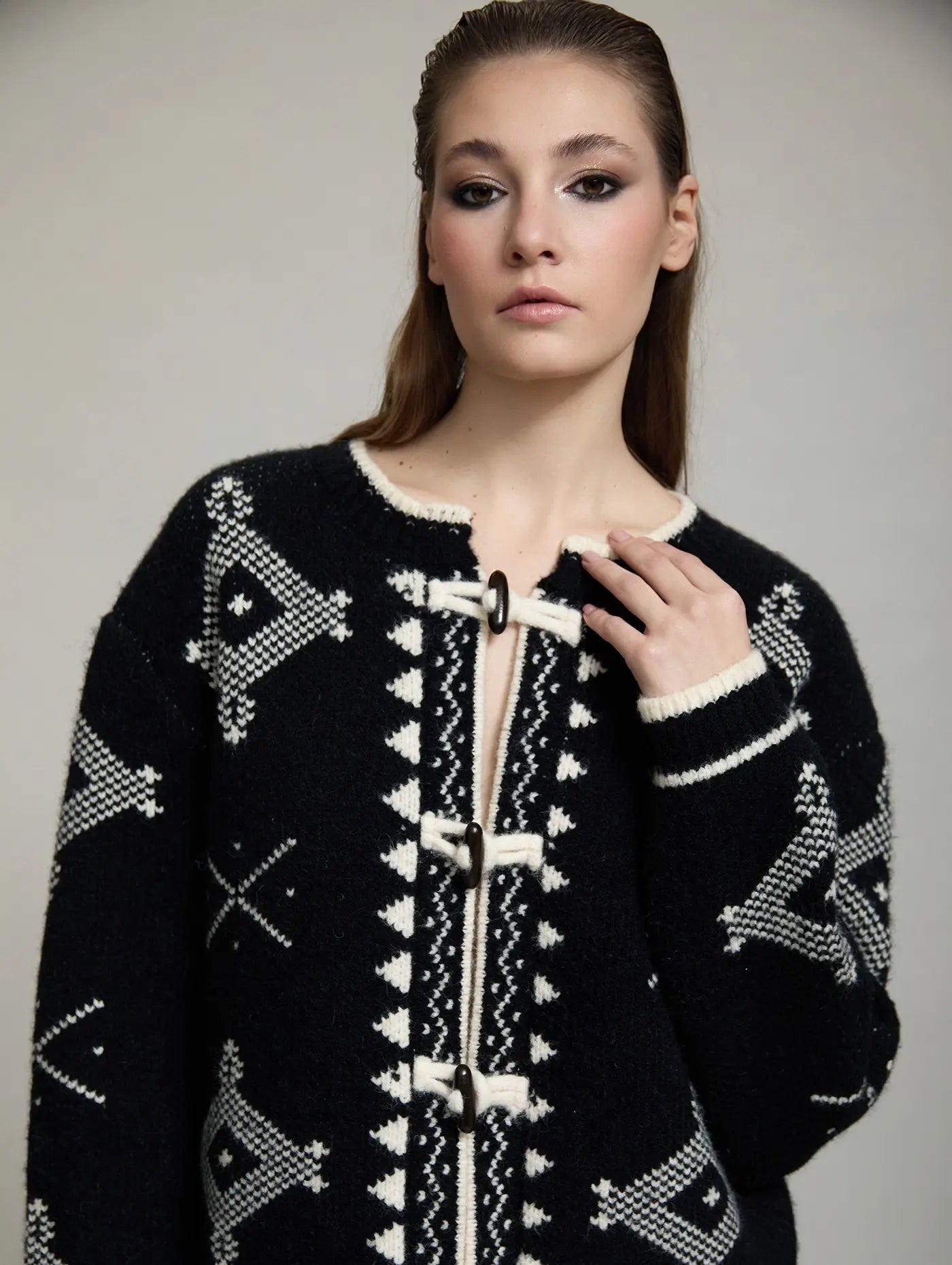 Detalle de la chaqueta de punto Zenda de SKATIE con estampado jacquard geométrico negro y crudo, ribete en contraste y cierres tipo alamar.