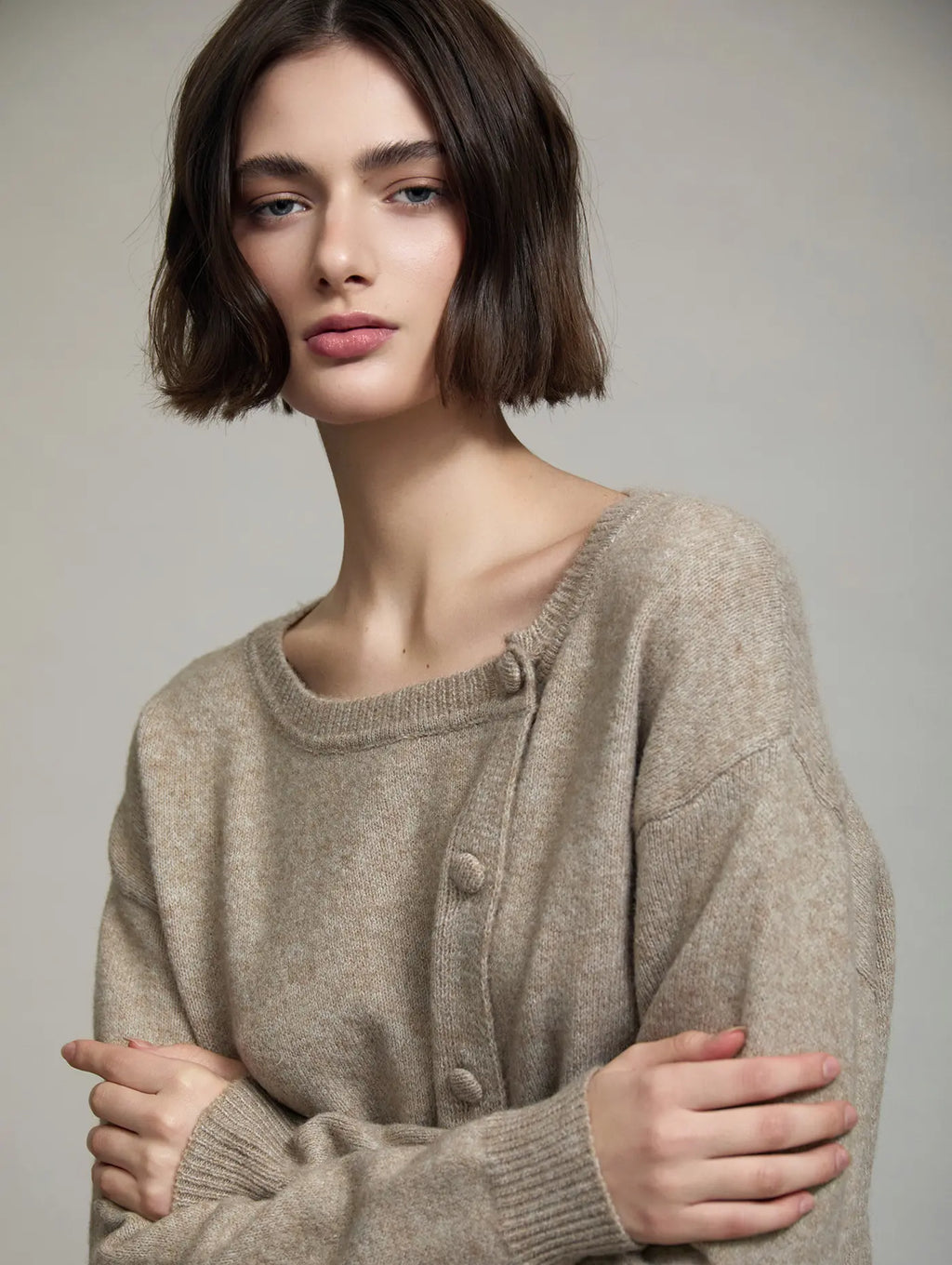 Detalle del Cardigan Sienna de SKATIE en punto beige mélange con escote redondo, hombro ligeramente caído y botonadura lateral diagonal con botones forrados al tono