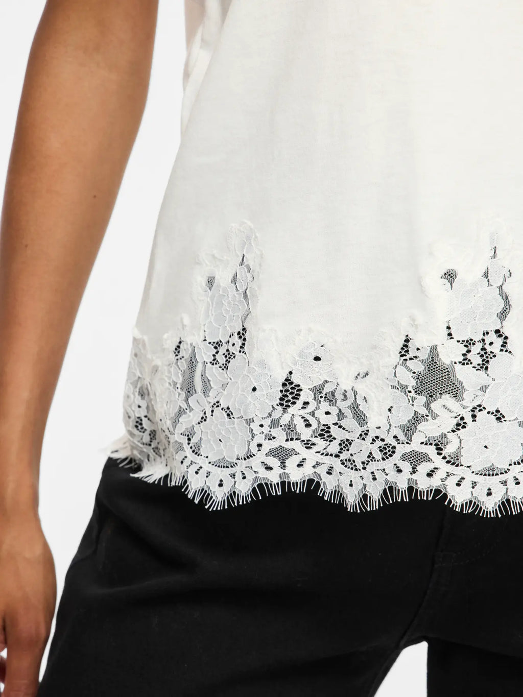 Detalle del bajo de camiseta blanca para mujer con encaje floral semitransparente y acabado de pestañas