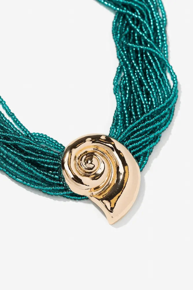 Detalle del collar Caracola Turquesa de Vilanova con cuentas turquesa y pieza central dorada inspirada en una caracola.