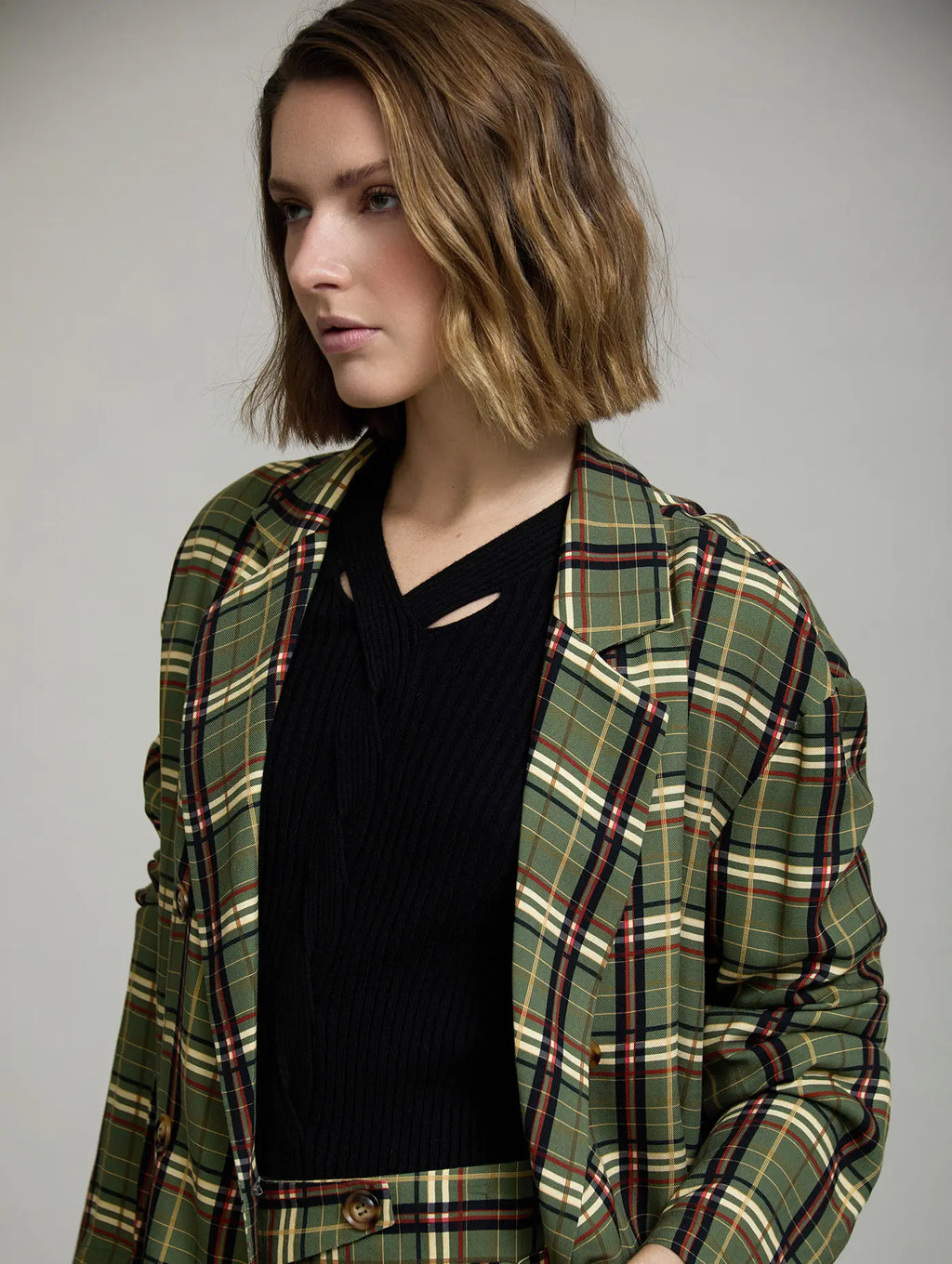 Detalle frontal de la Americana Kensington de cuadros verde con solapas amplias, doble botonadura y estampado tartán en crudo, negro, rojo y mostaza
