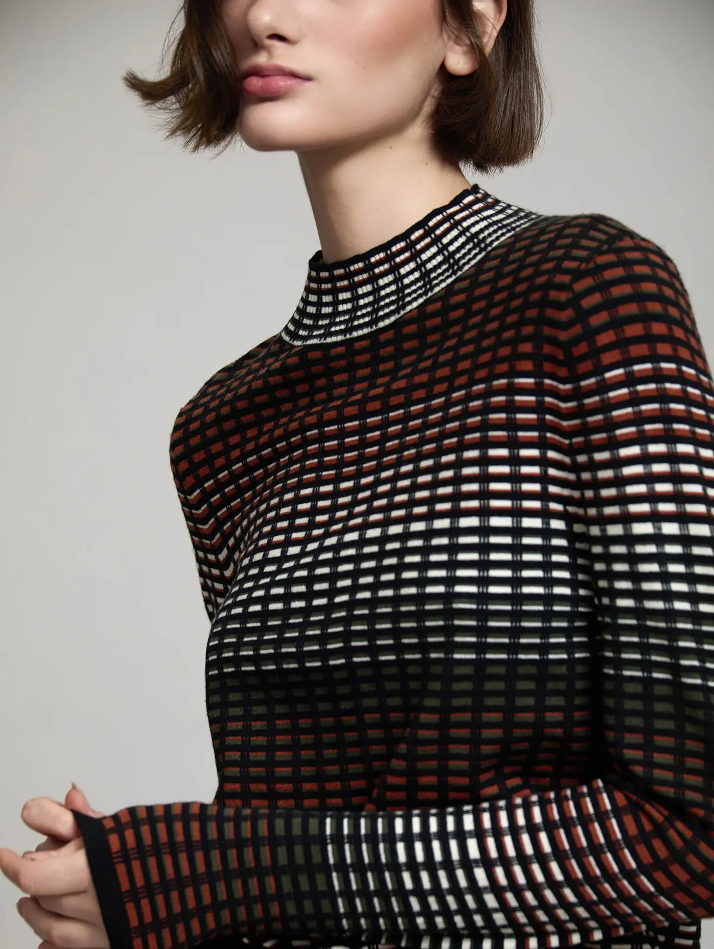 Detalle del jersey Margot de SKATIE de punto con diseño geométrico de cuadros, cuello alto y combinación de negro, crudo, verde oliva y teja