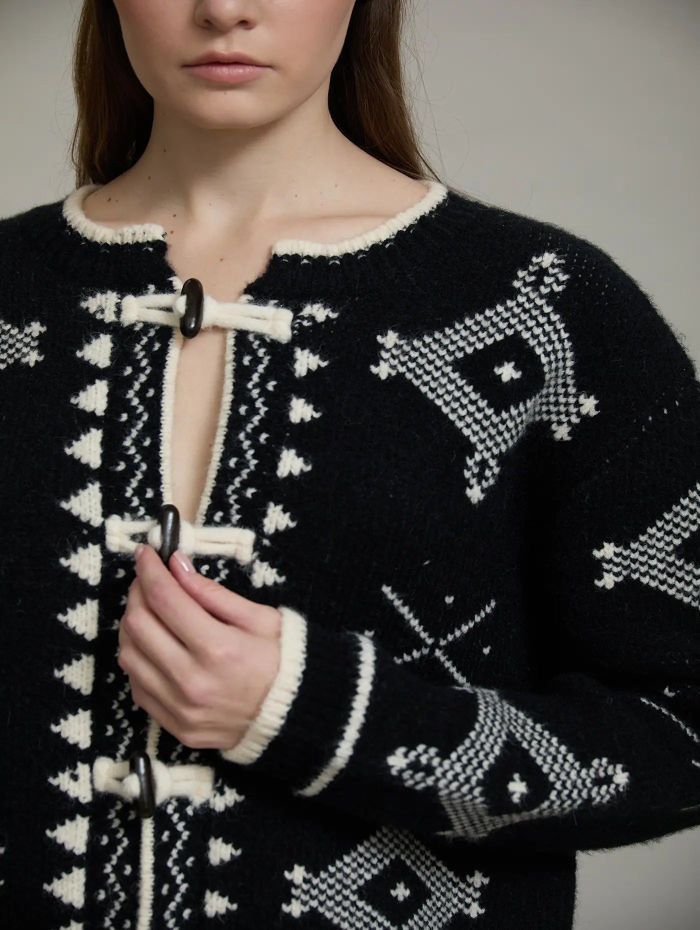 Vista frontal de la chaqueta Zenda de SKATIE en punto jacquard negro y crudo con motivos geométricos, cuello redondo y cierres tipo alamar.