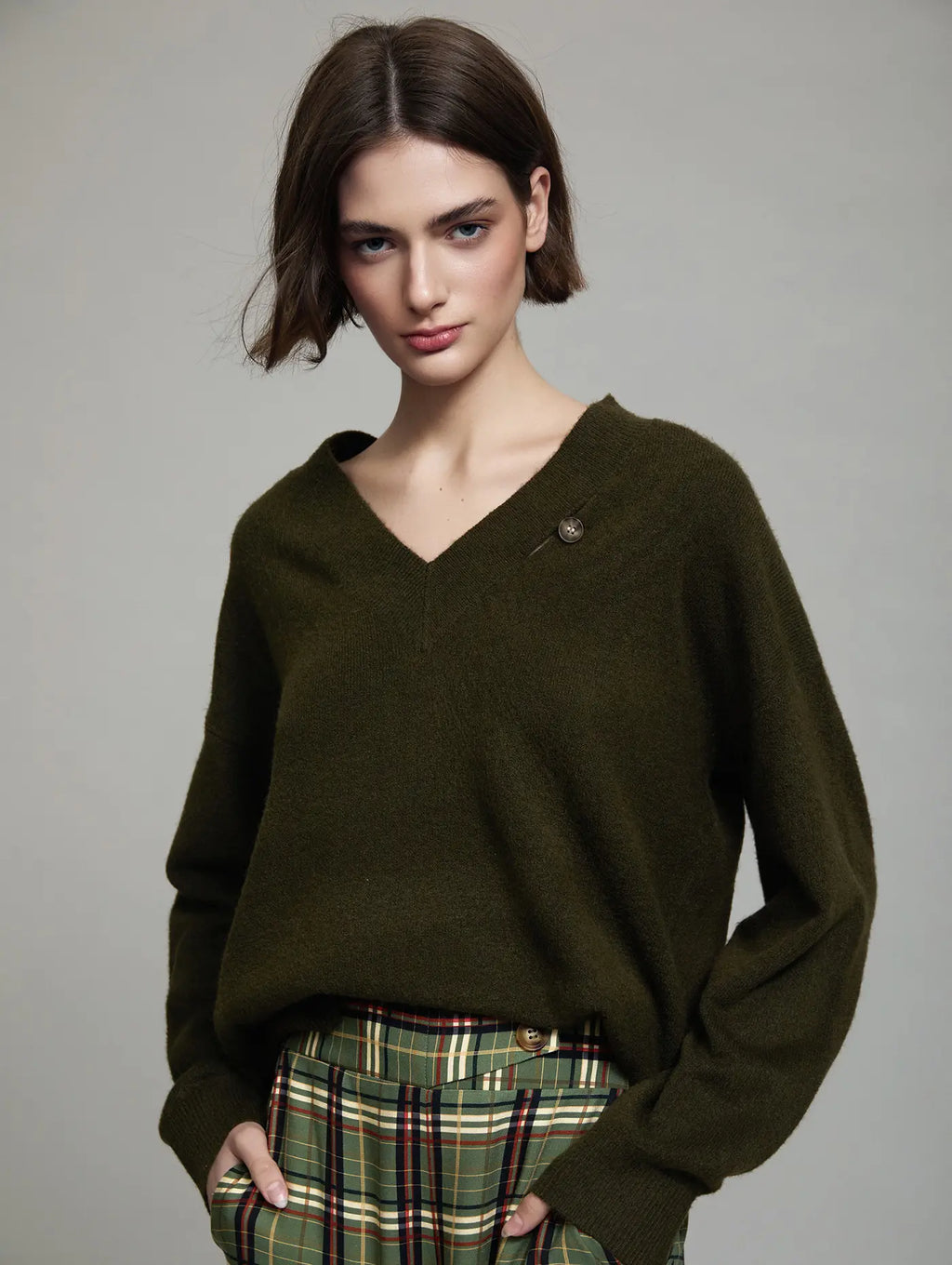 Jersey Cambridge verde oliva de mujer con cuello pico, manga larga, corte relajado, botón decorativo y coderas camel, vista frontal