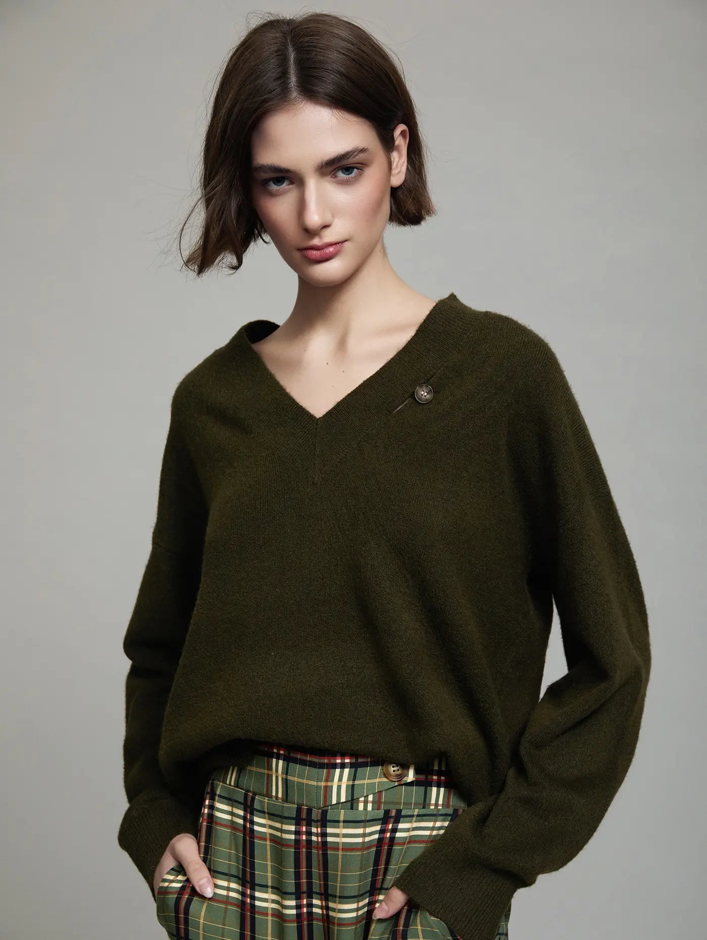 Jersey Cambridge verde oliva de mujer con cuello pico, manga larga, corte relajado, botón decorativo y coderas camel, vista frontal