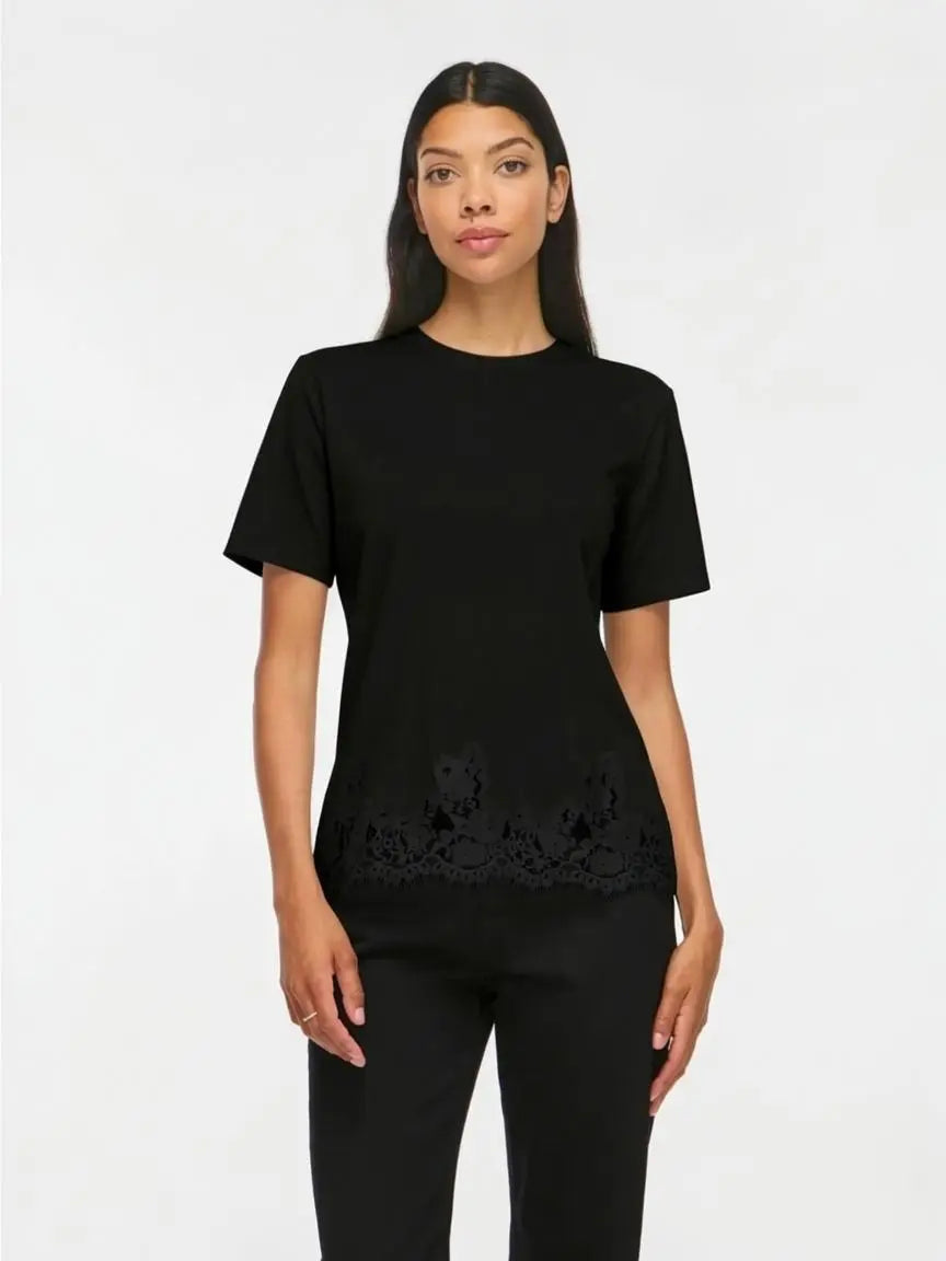 Modelo con camiseta negra de manga corta y cuello redondo con detalle de encaje floral negro semitransparente en el bajo
