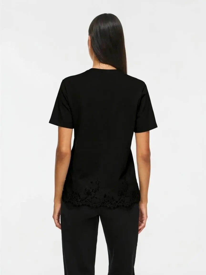 Modelo vista de espaldas con camiseta negra de manga corta y detalle de encaje floral decorativo alrededor del bajo