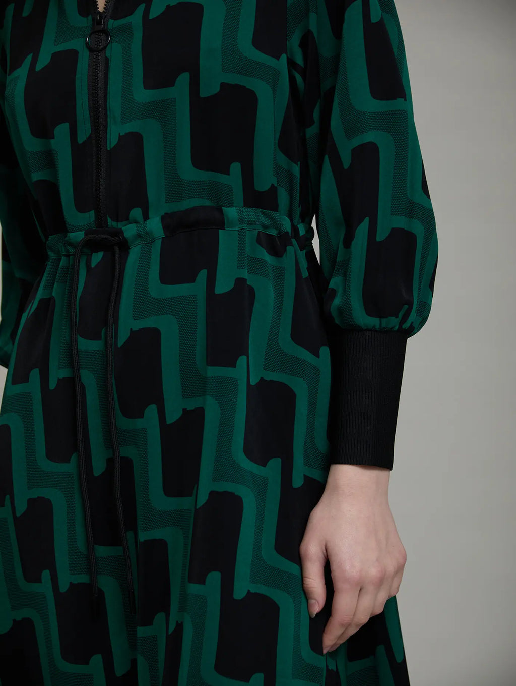 Detalle del vestido Sylvie de SKATIE con estampado geométrico verde y negro, cintura regulable con cordón y puños anchos de punto negro