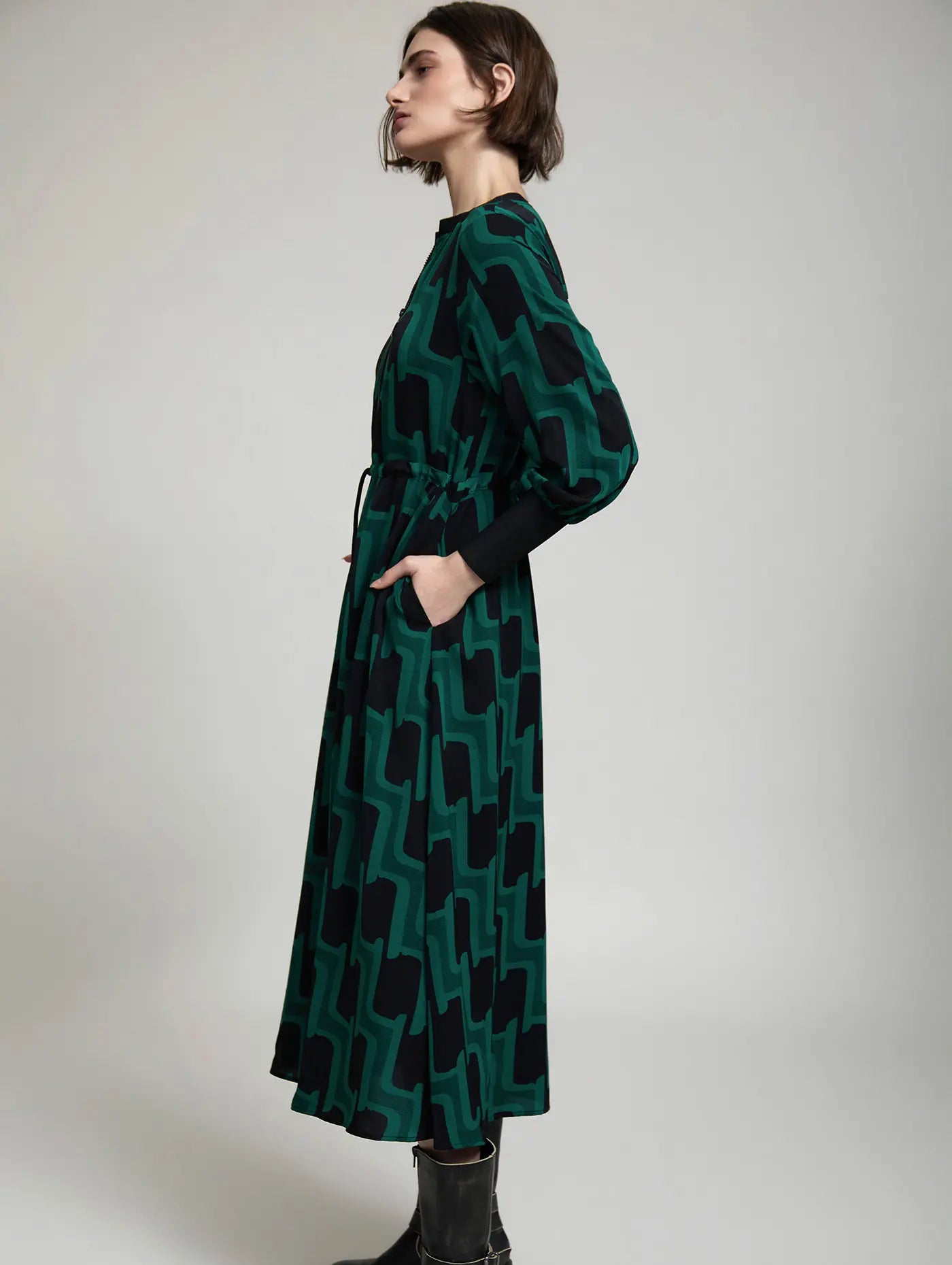 Vista lateral del vestido midi Sylvie de SKATIE en verde y negro con estampado geométrico, manga abullonada, puños negros y falda fluida