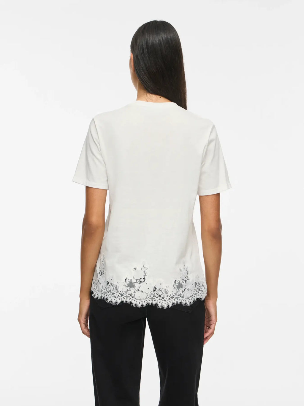 Modelo vista de espaldas con camiseta blanca de manga corta y detalle de encaje floral decorativo alrededor del bajo