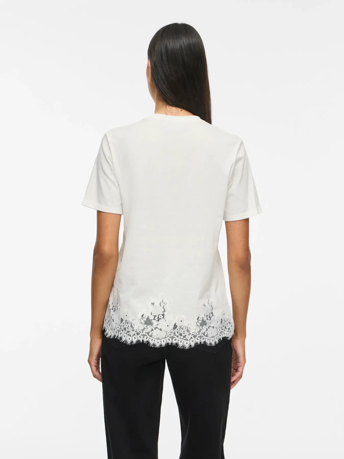 Modelo vista de espaldas con camiseta blanca de manga corta y detalle de encaje floral decorativo alrededor del bajo