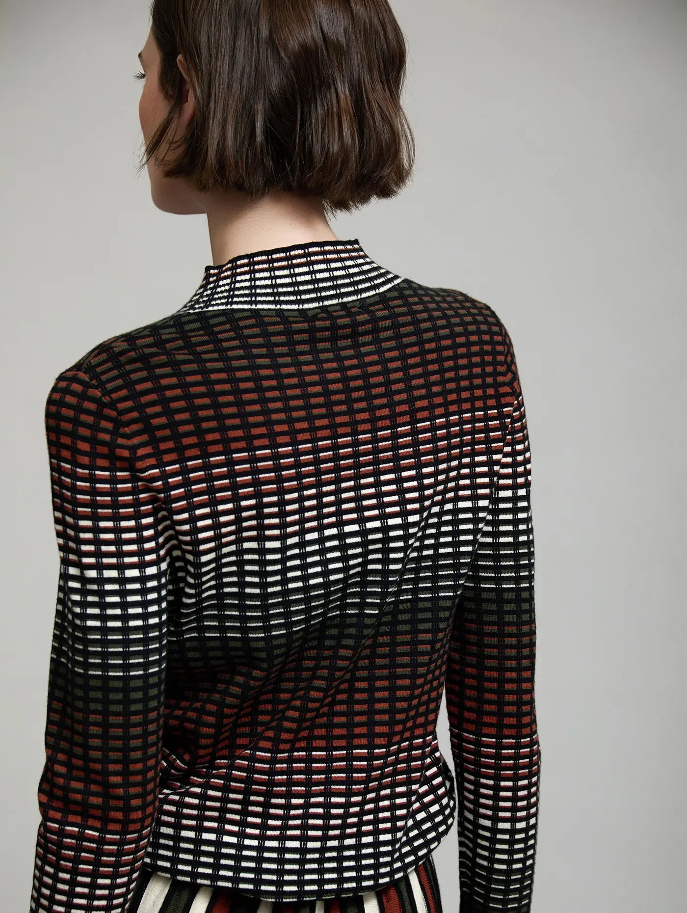 Vista trasera del jersey de punto Margot de SKATIE con diseño de cuadros multicolor en negro, crudo, verde oliva y teja